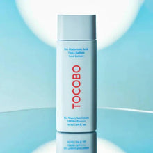 Tocobo sunscreen bottle on a reflective surface with a blue gradient background